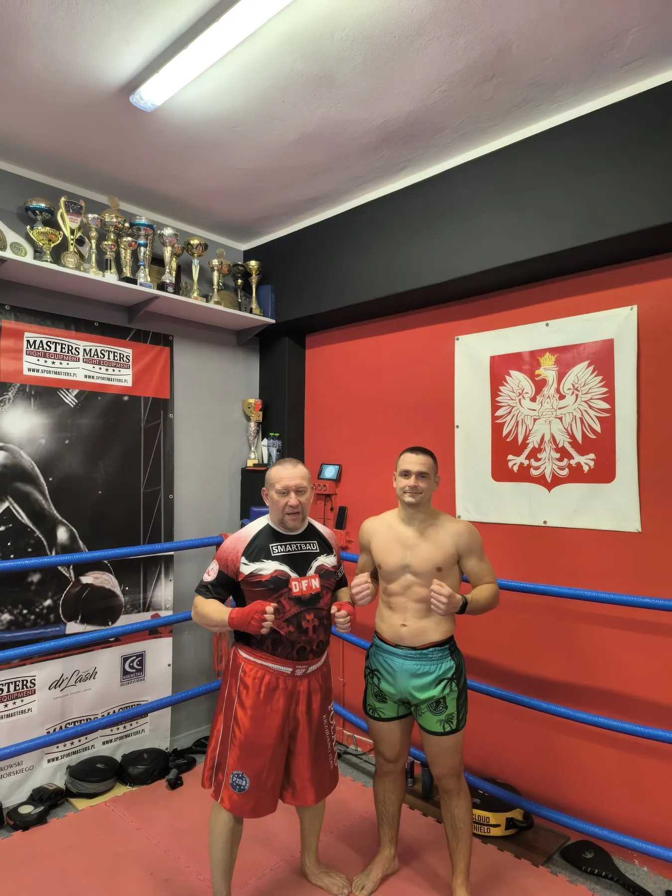 Trener i zawodnik w ringu klubowym, na ścianie godło Polski
