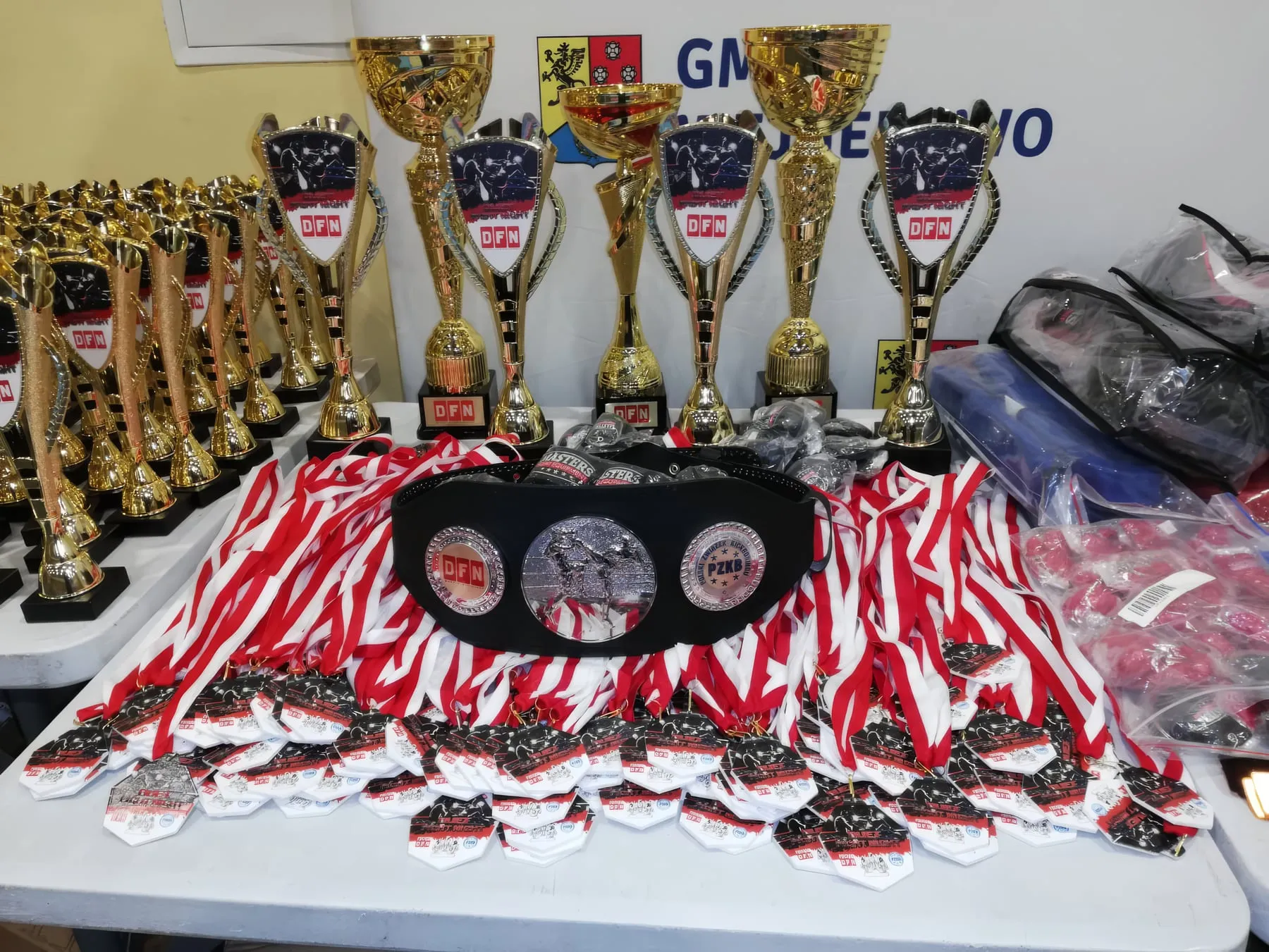 Stół z pucharami, medalami i pasami przygotowanymi na dekorację
